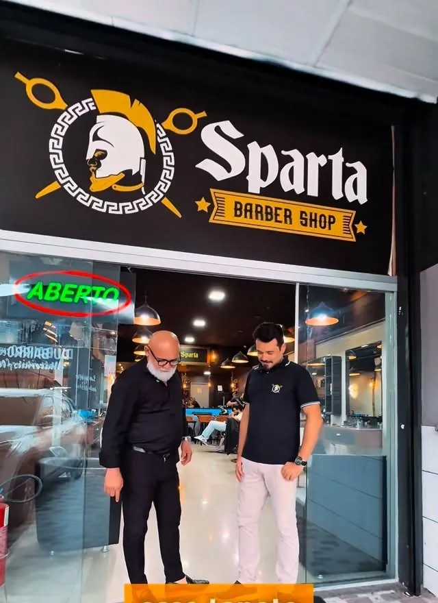 Fachada da Sparta Barber Shop com o letreiro iluminado e o tapete com o emblema